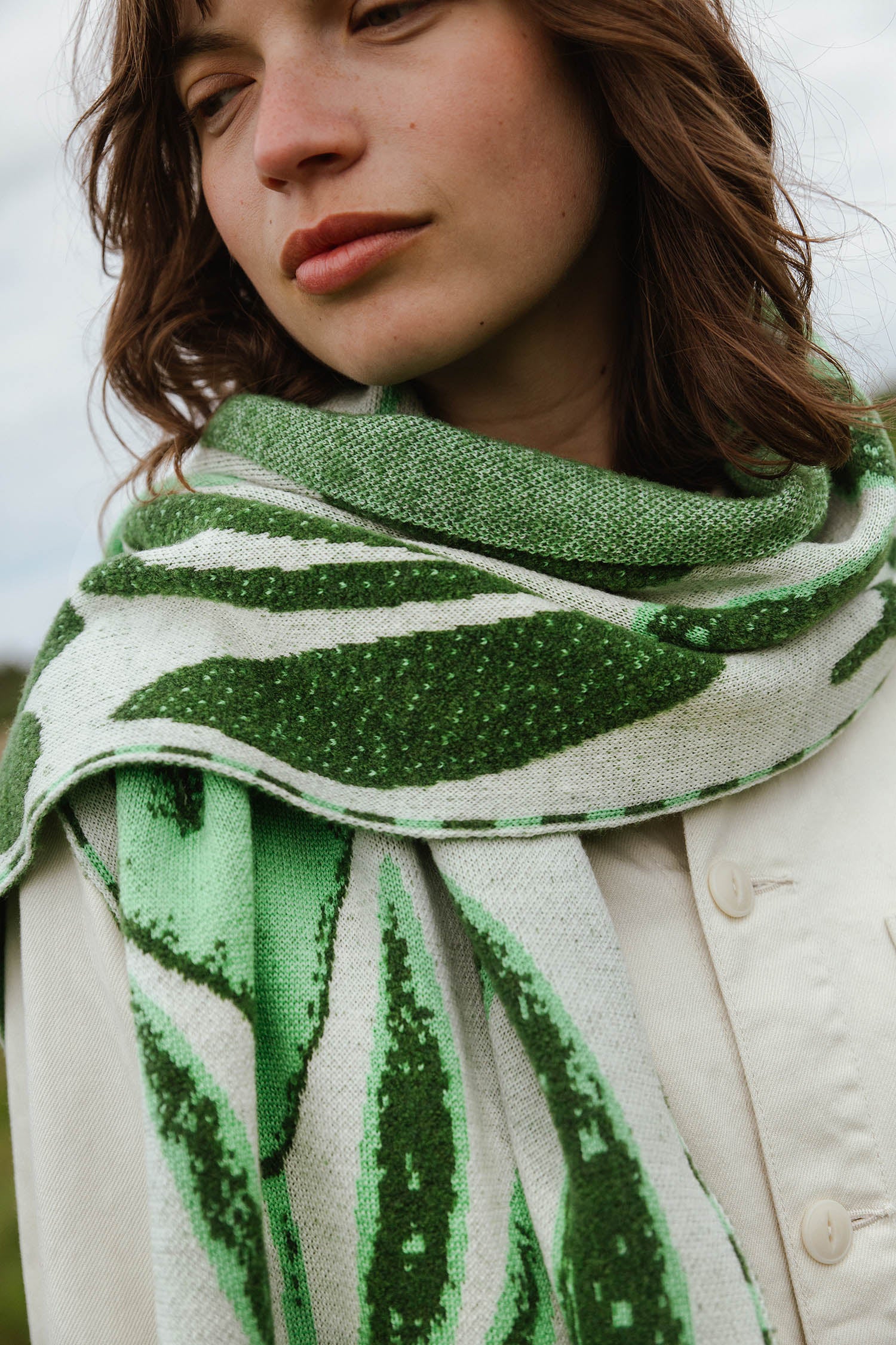 A cream and green knitted scarf with a leaf pattern.
