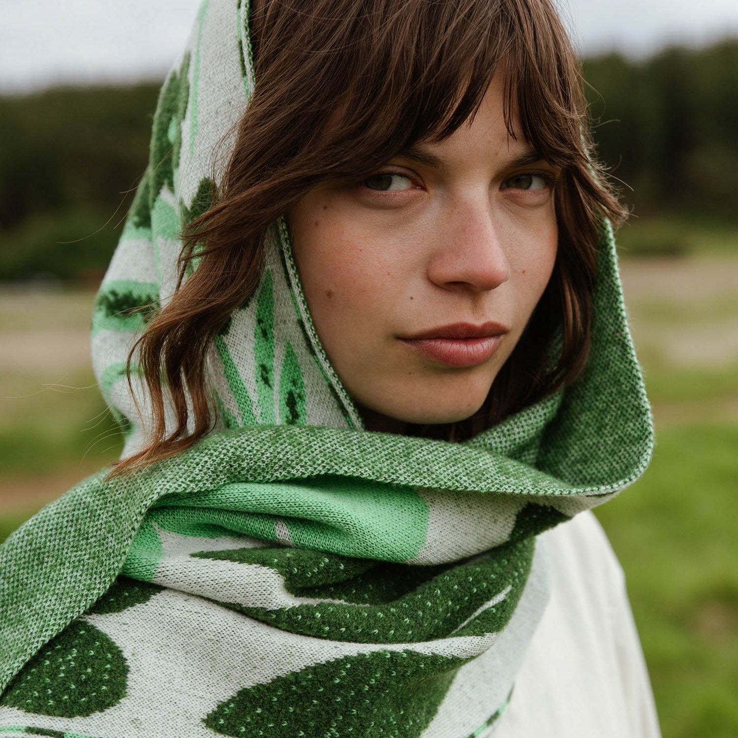 Green and off-white knitted scarf with leaf pattern, worn as a hood.