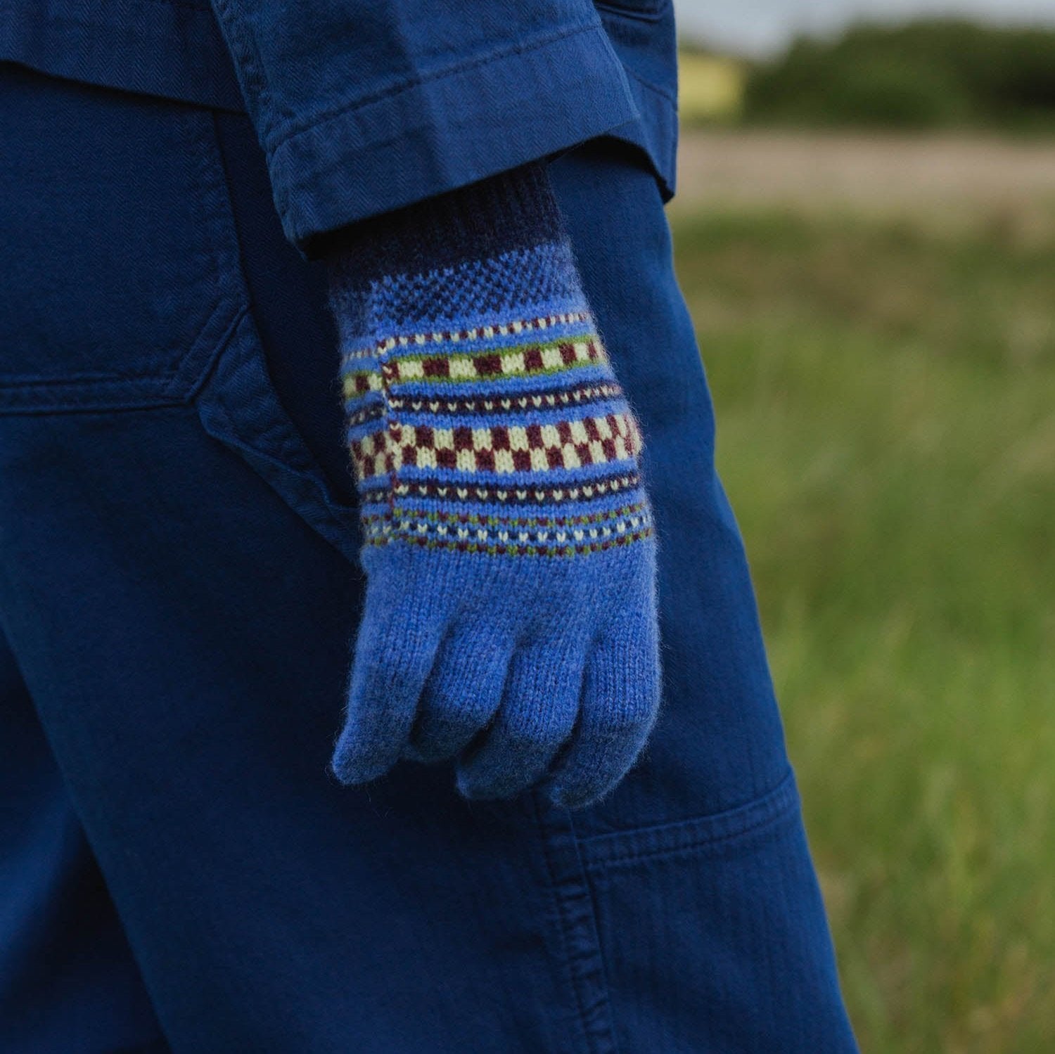 Blue knitted gloves with a patterned cuff featuring brown, cream, and green stripes.