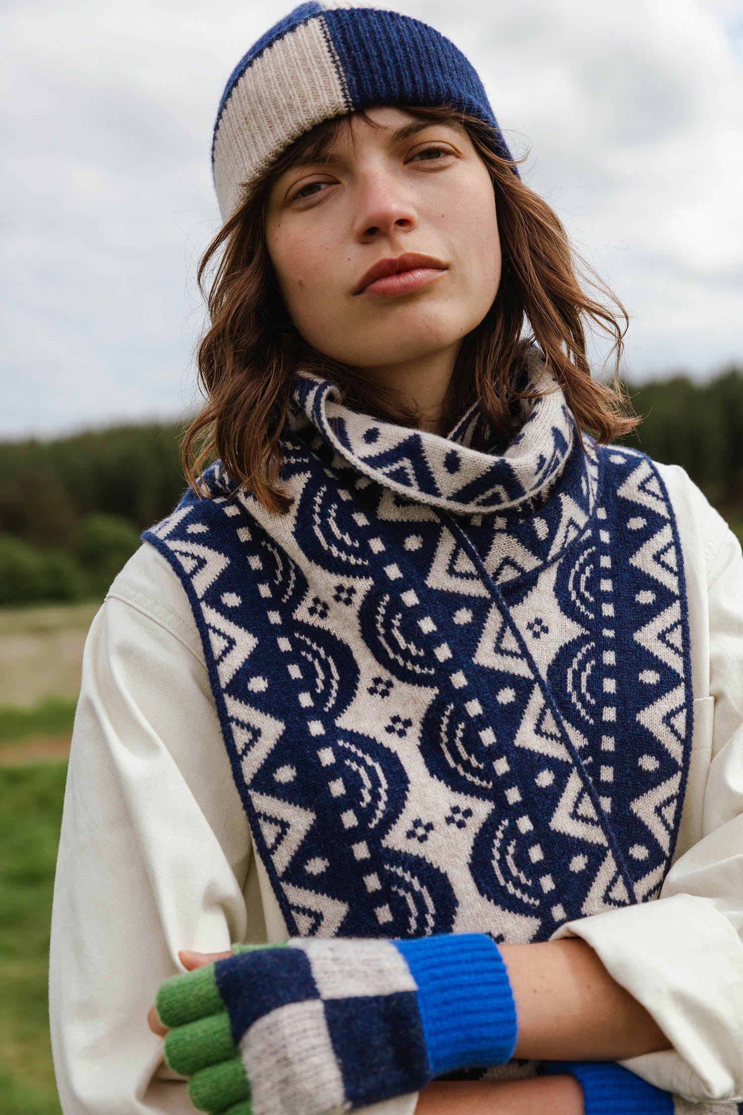 Woman wearing a blue and cream patterned knit scarf, matching beanie, and multicolored fingerless gloves.