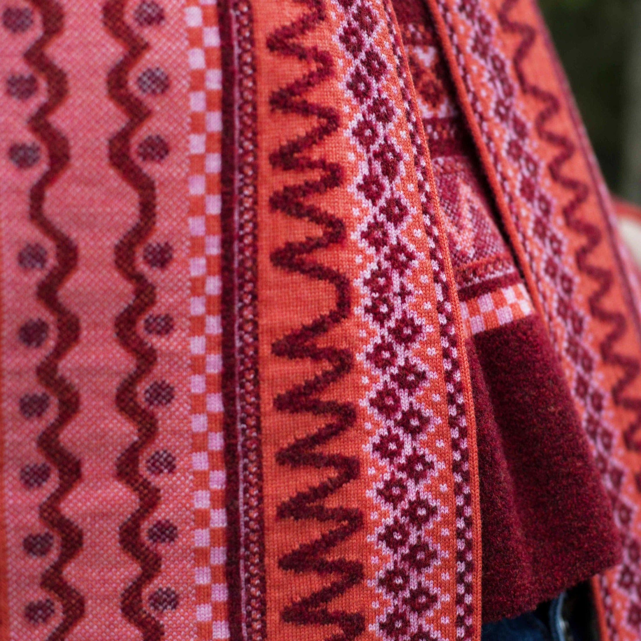 Close-up of a knitted garment featuring intricate, multicolored patterns in shades of red, pink, and burgundy.