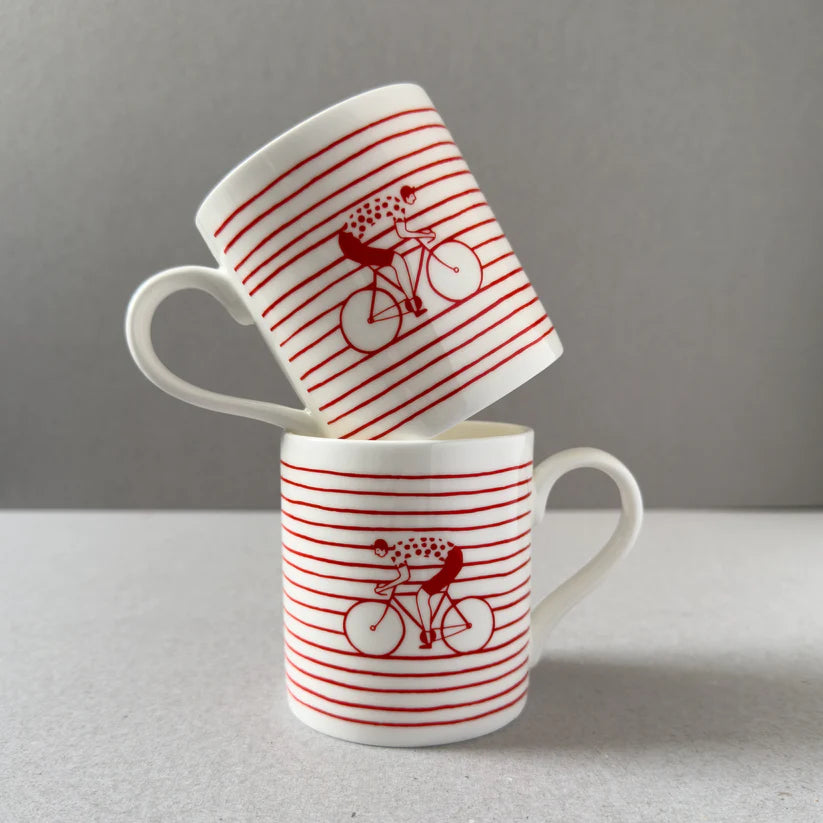 Two white mugs stacked, featuring red horizontal stripes and a cyclist design.