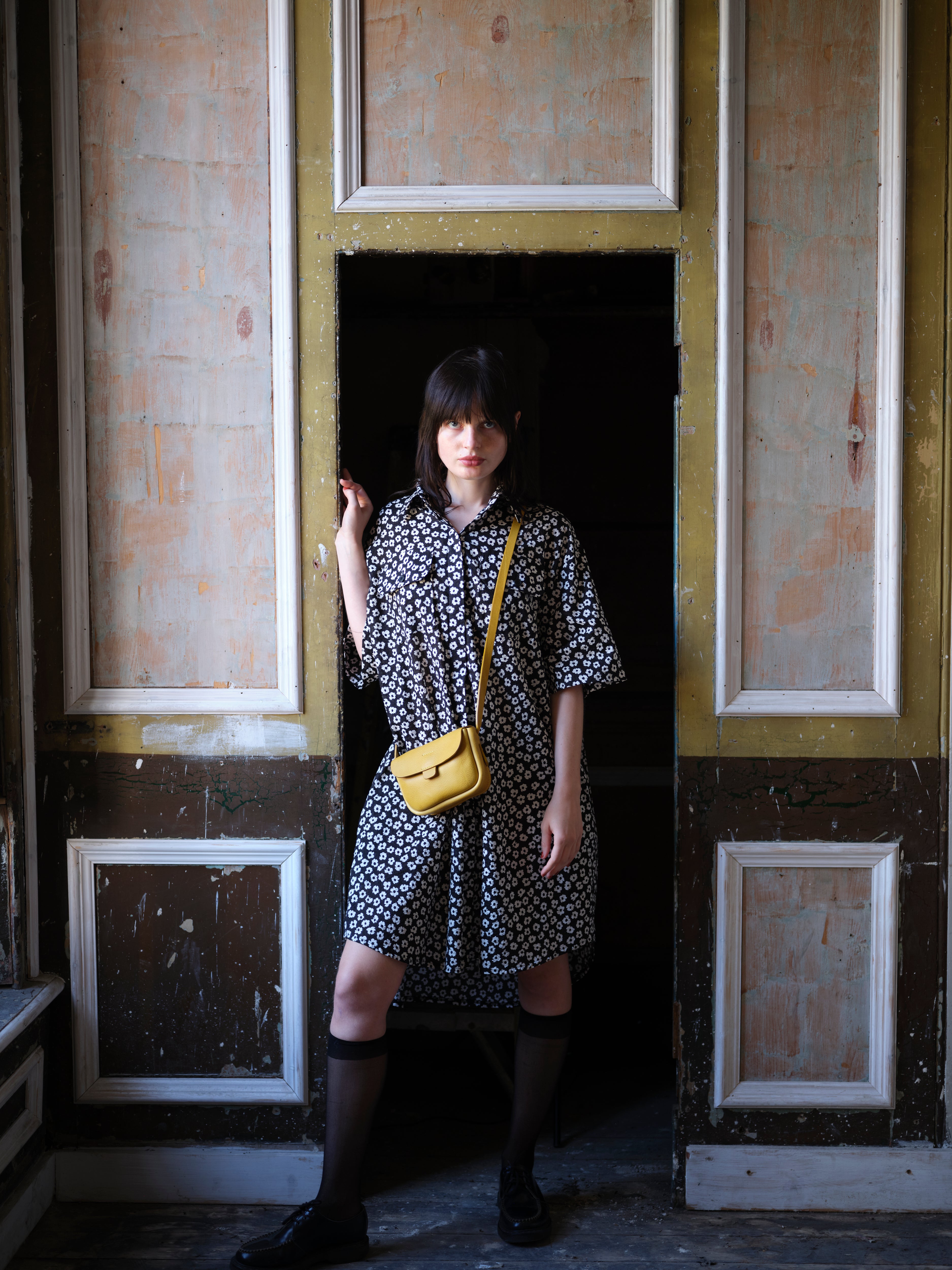 A woman in a black and white floral dress wears a mustard-yellow crossbody bag.