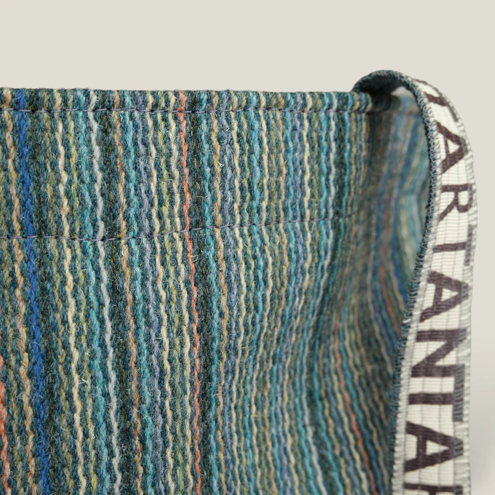 Close-up of a striped, teal and beige woven textile bag with a fabric strap. The bag shows visible stitching.