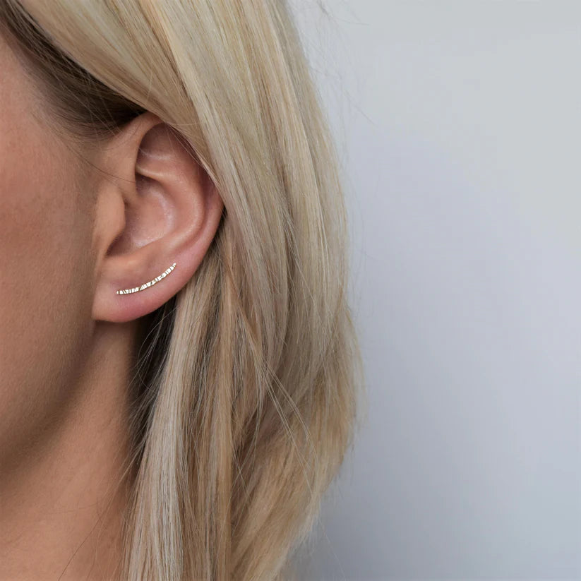 Gold ear crawler earrings with a textured, curved design.
