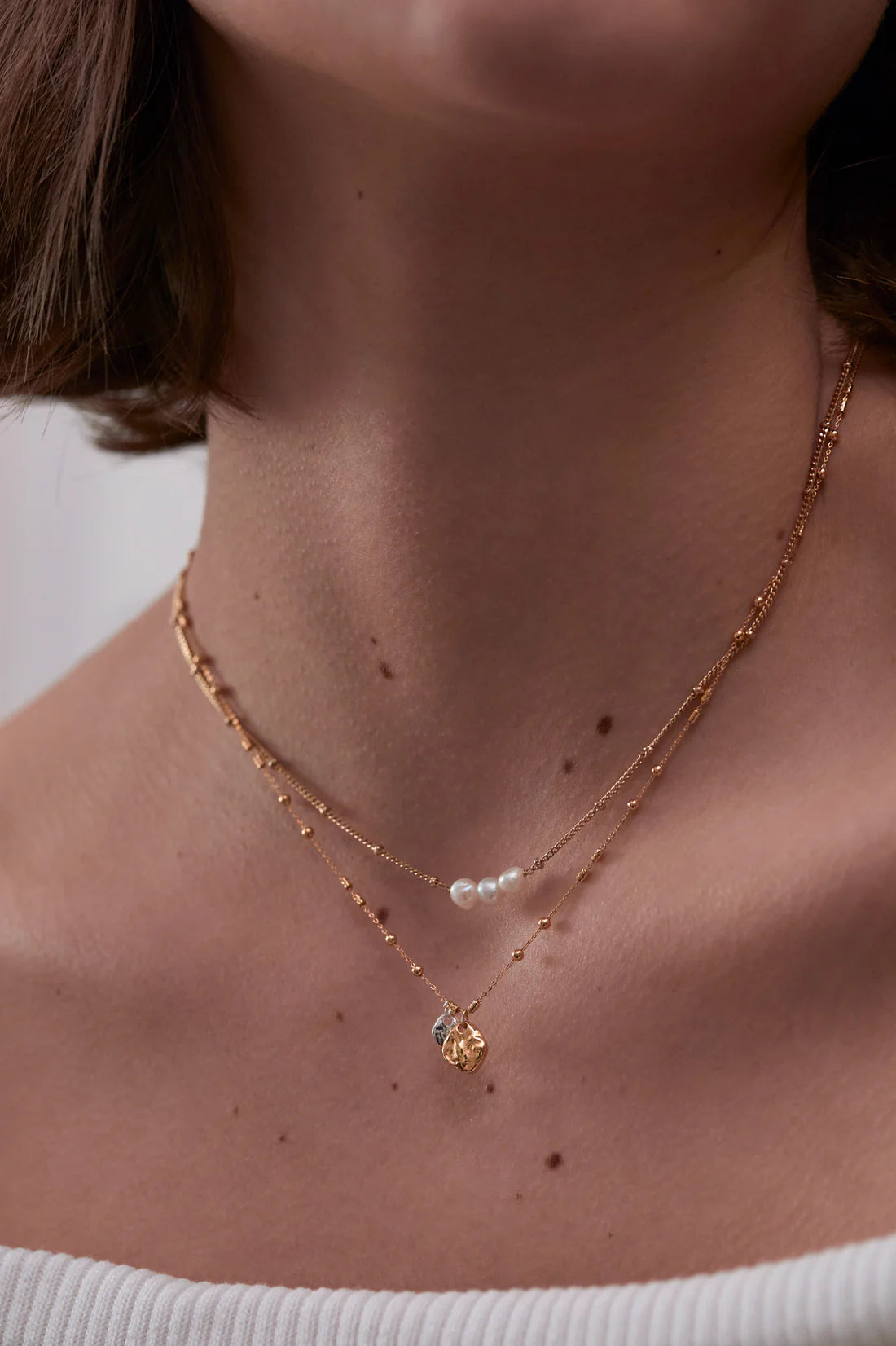 Gold layered necklace featuring small beads, three pearls, and a textured gold charm.