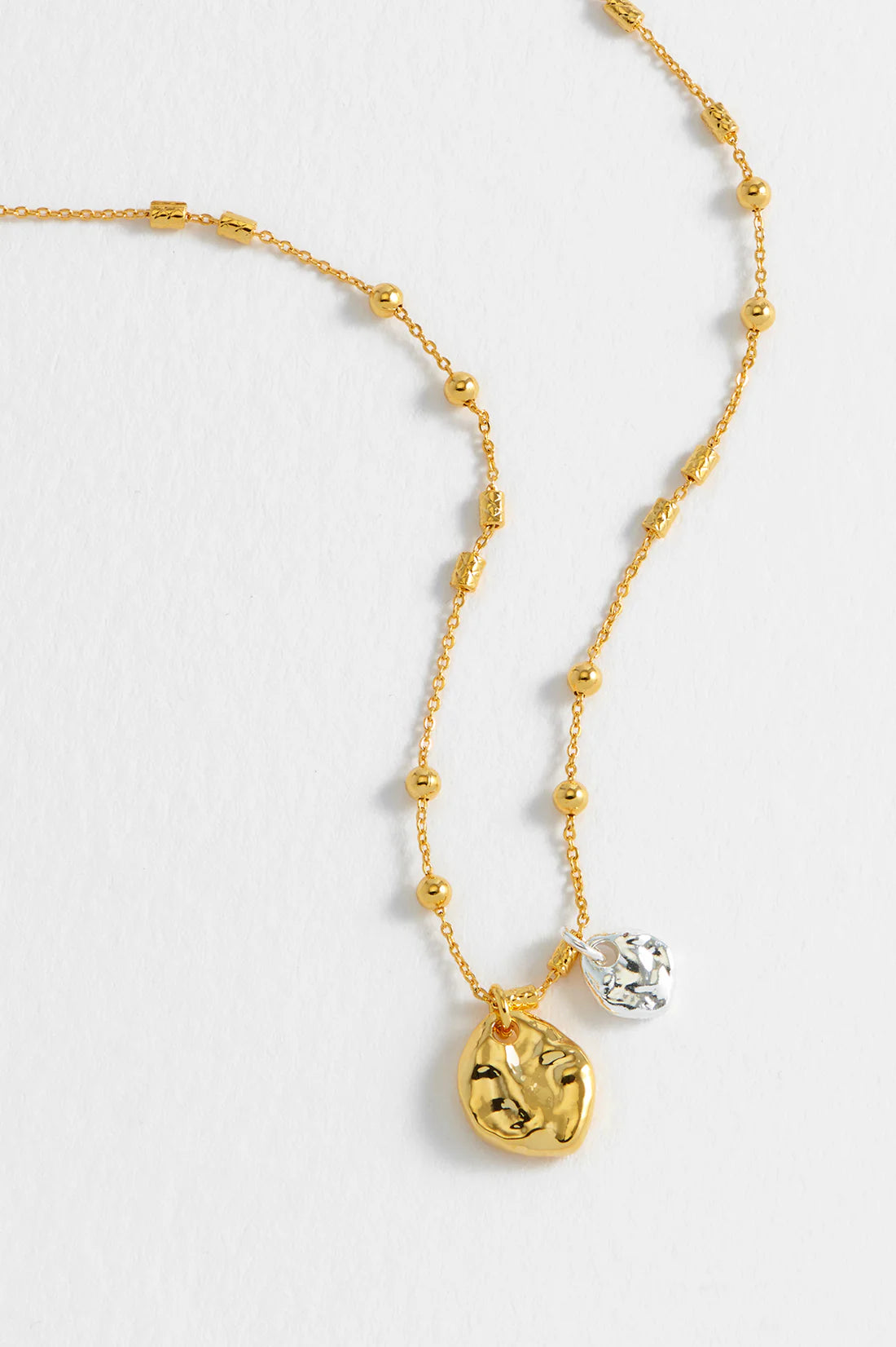 Gold beaded necklace with two textured pendant charms; one gold, one silver.