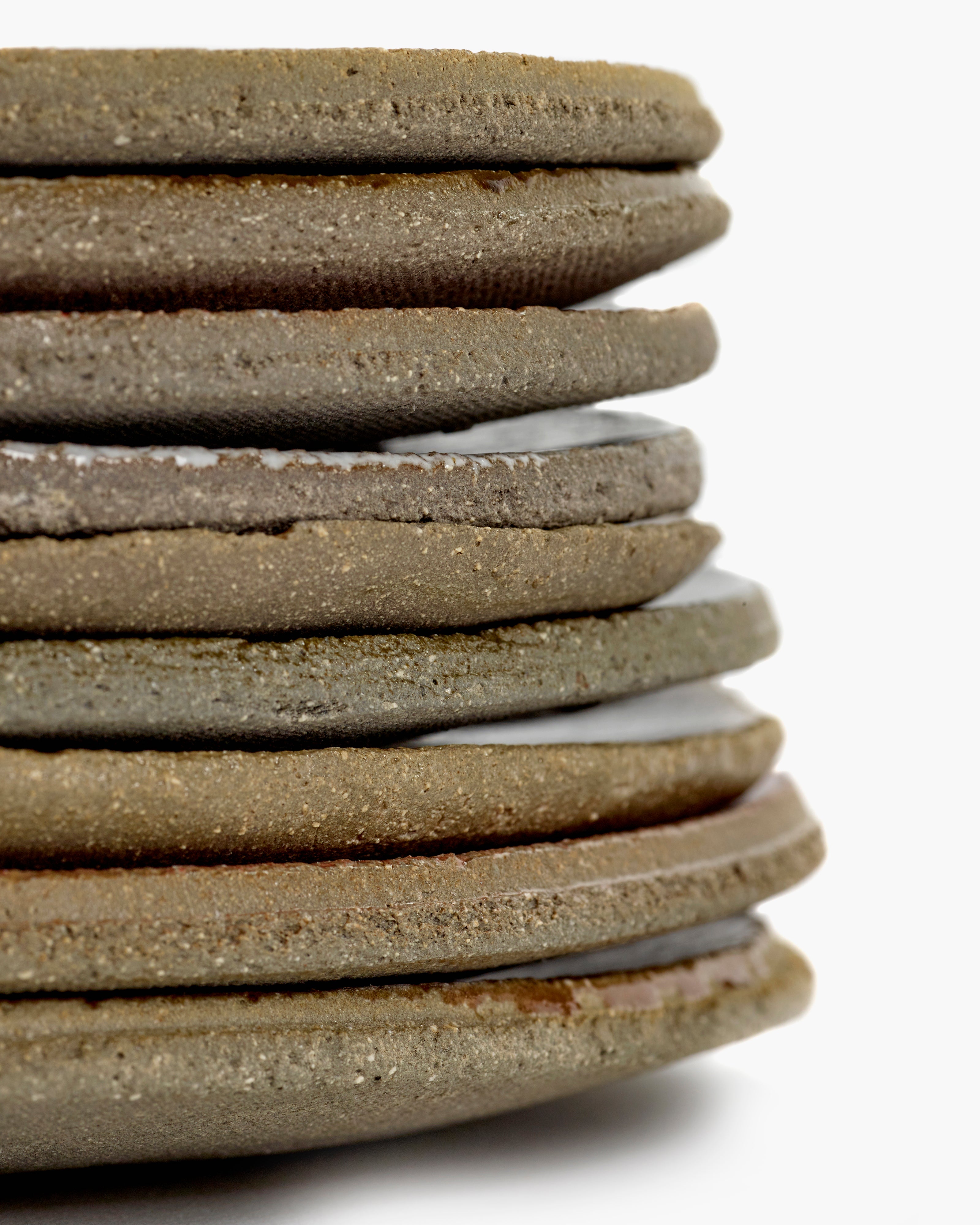 Stack of round, textured ceramic coasters in varying shades of brown and beige, with visible white glaze between some layers.