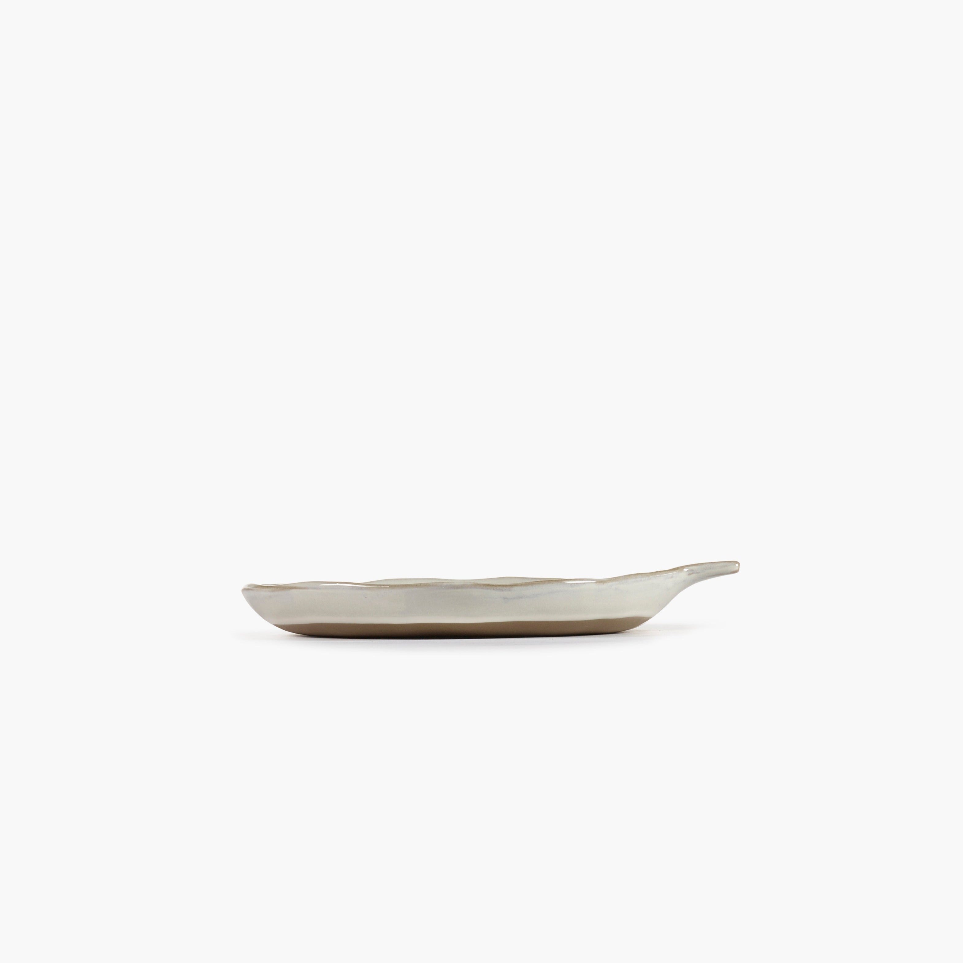 Off-white ceramic dish with a light brown base and a small handle.  The dish has an organic, leaf-like shape.
