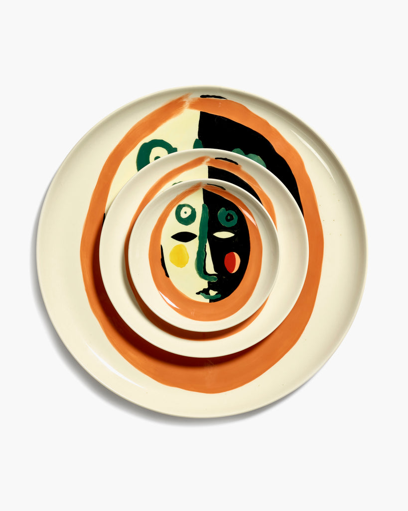 three plates, one on top of another, with a painting of a face in black, orange and green, designed by British-Israeli chef Yotam Ottolenghi, for Belgian design brand Serax.