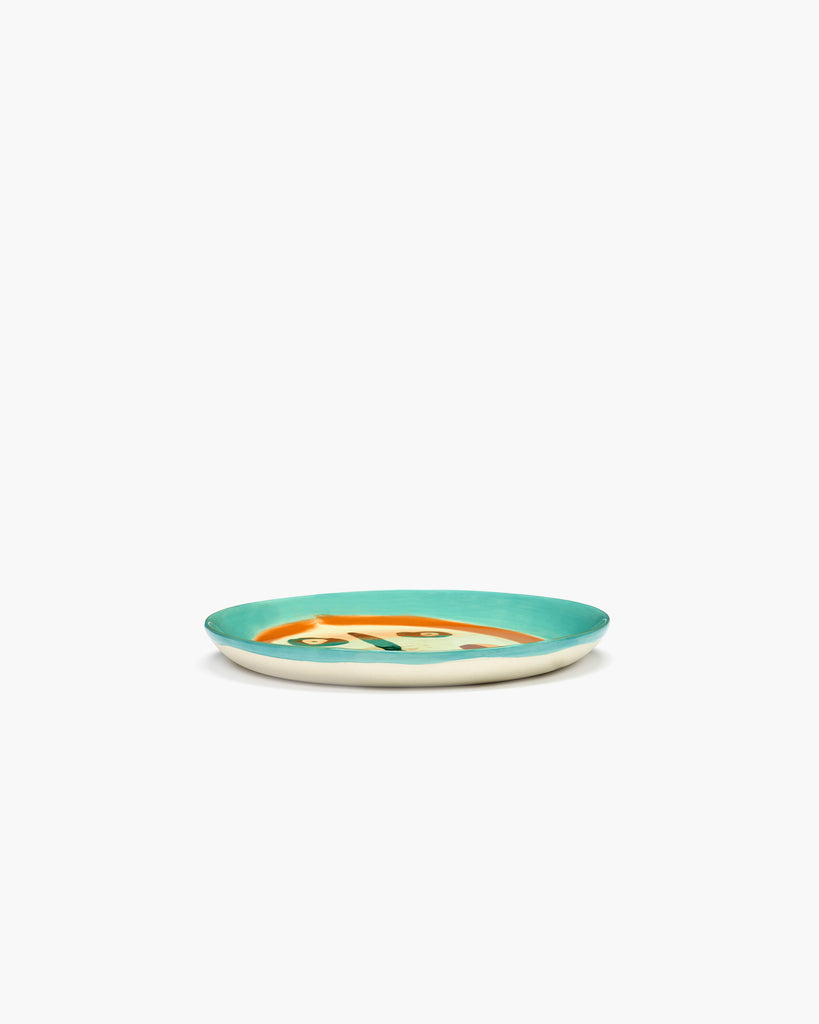 cream coloured plate with a painting of a face in deep blue, orange and green, designed by British-Israeli chef Yotam Ottolenghi, for Belgian design brand Serax.