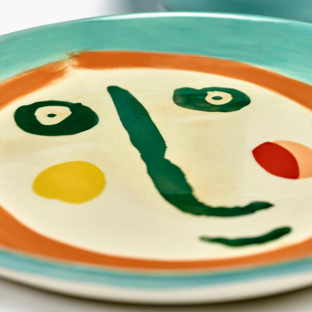 cream coloured plate with a painting of a face in deep blue, orange and green, designed by British-Israeli chef Yotam Ottolenghi, for Belgian design brand Serax.
