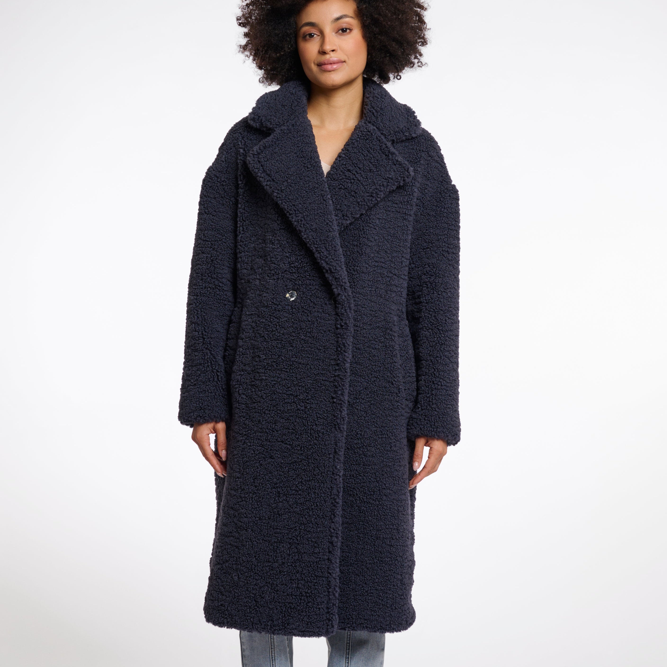 A woman models a double-breasted, teddy coat in night grey with a large lapel collar and side slit pockets.