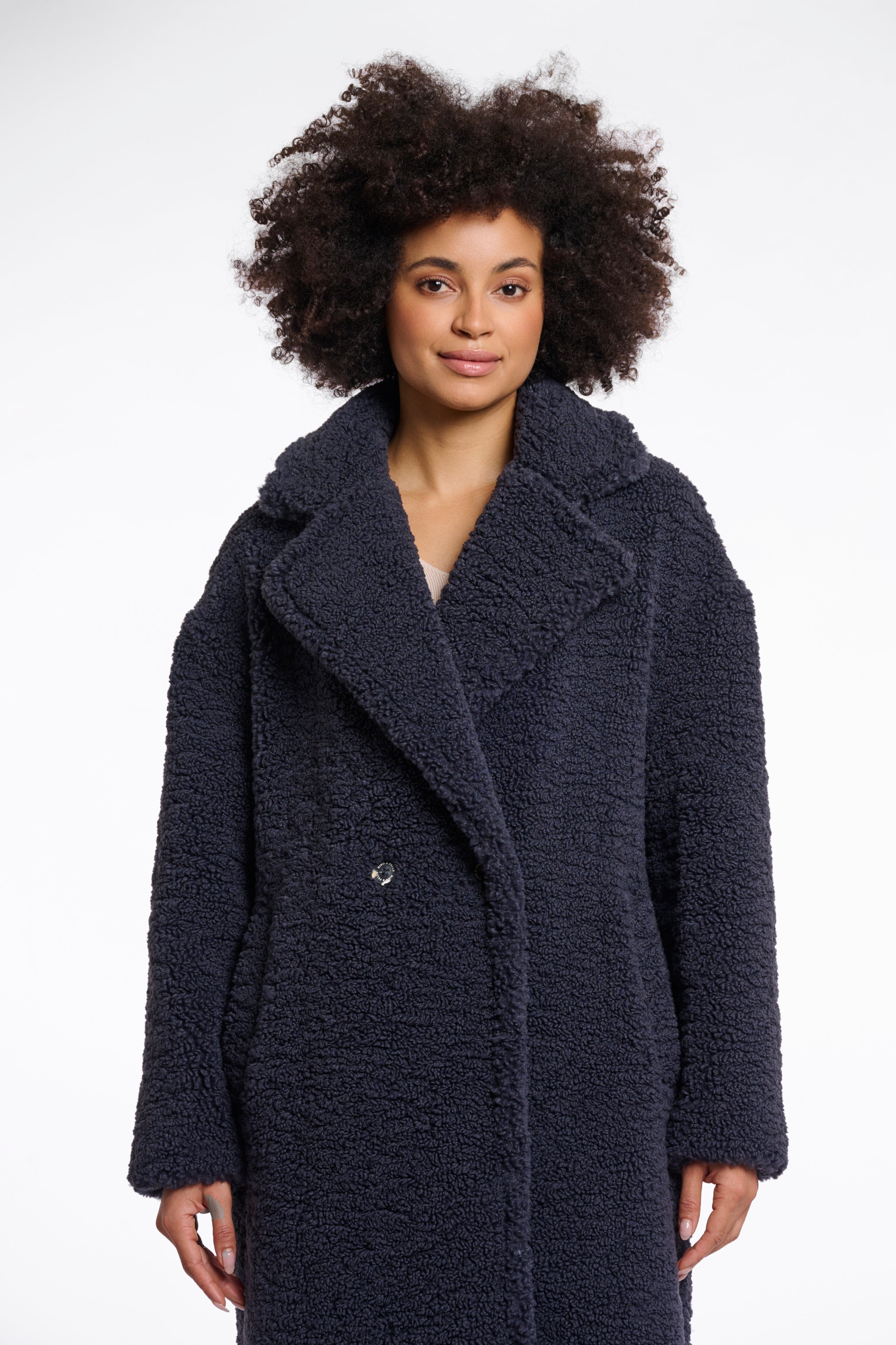 A woman models a double-breasted, teddy coat in night grey with a large lapel collar and side slit pockets.