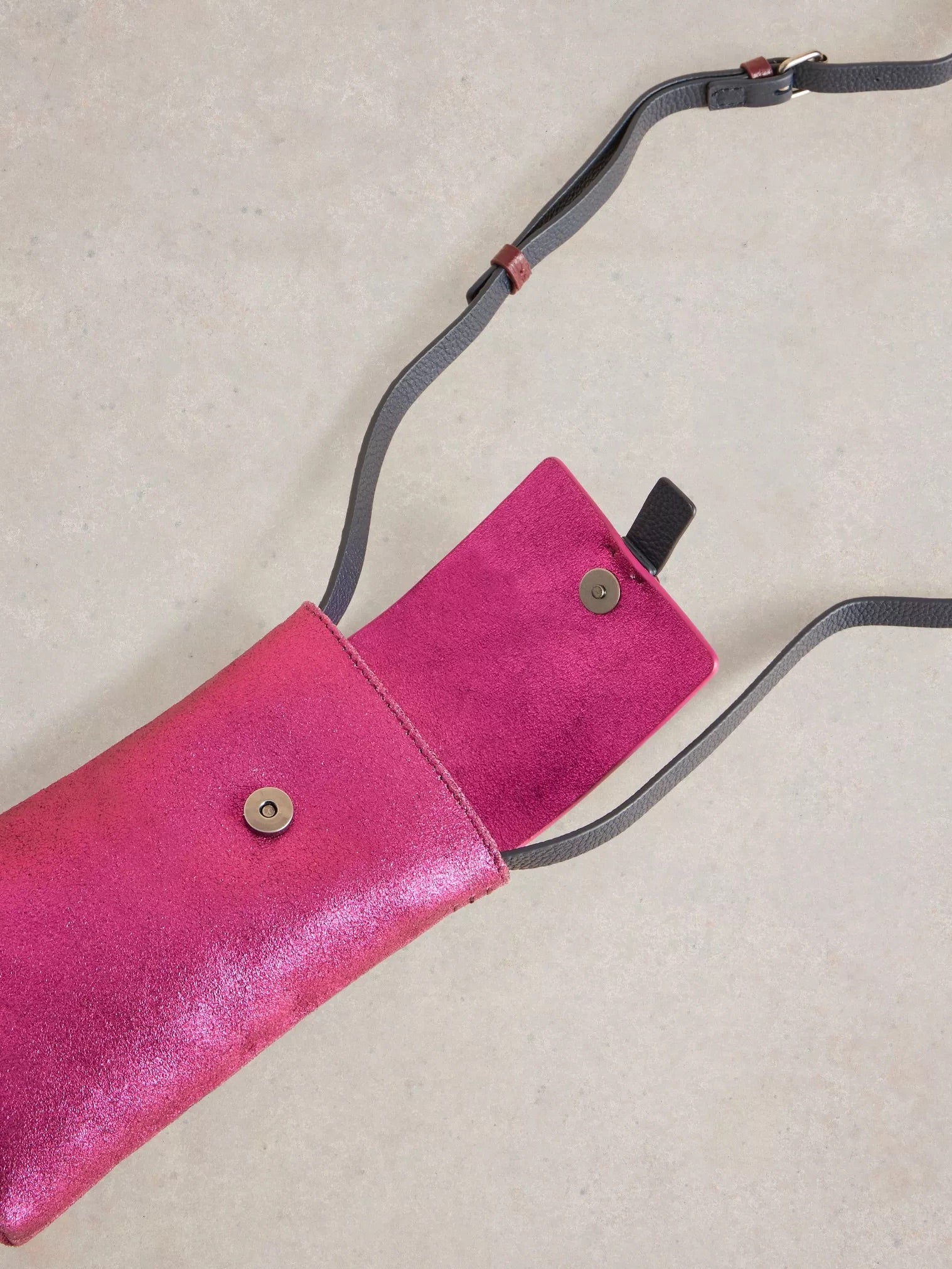 Pink metallic crossbody bag with a black leather strap and magnetic closure.