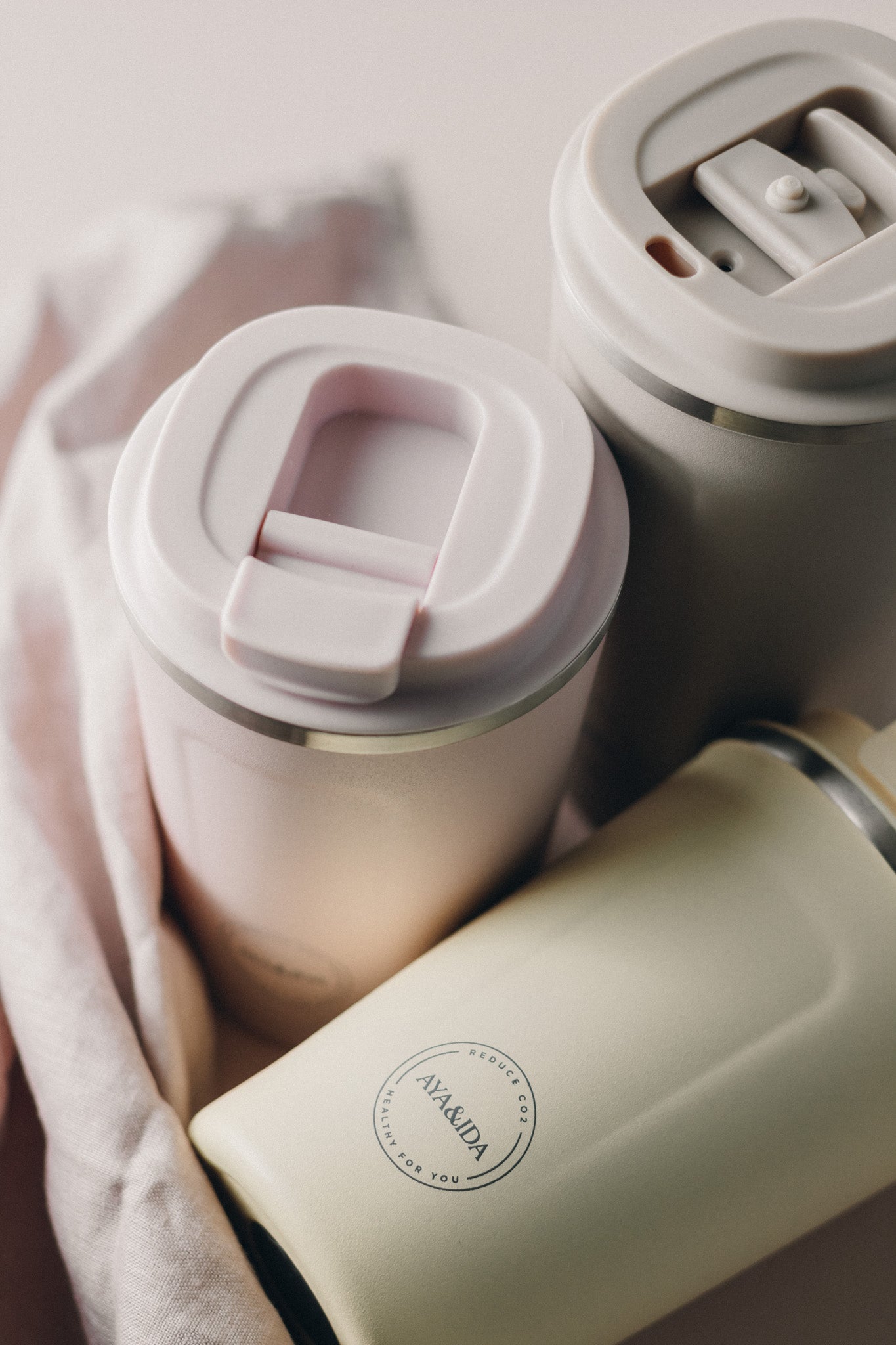 Three pastel-colored reusable coffee cups; one light pink, one beige, and one off-white.
