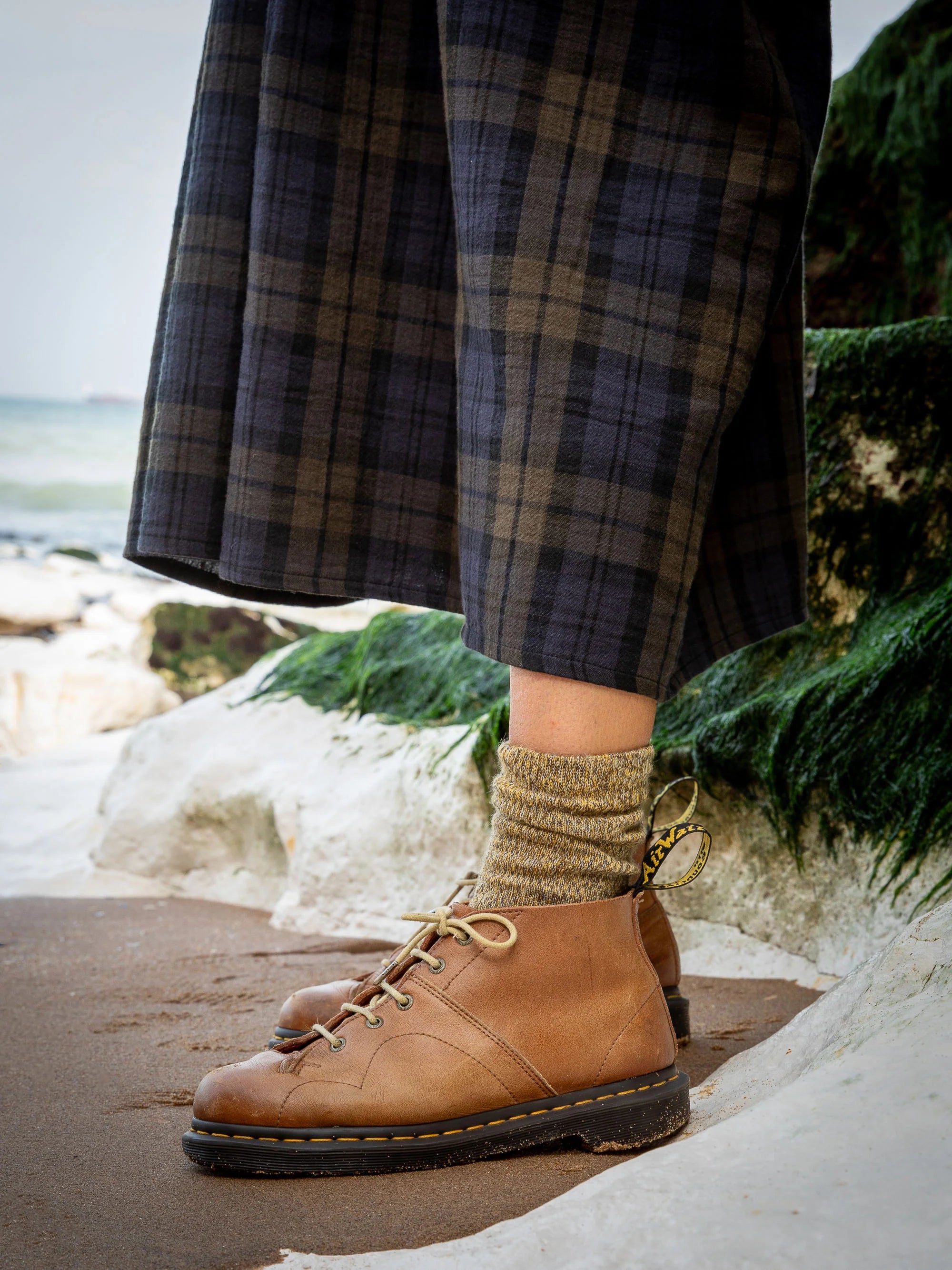 Brown leather Dr. Martens ankle boots with cream laces, worn with mustard-colored socks.
