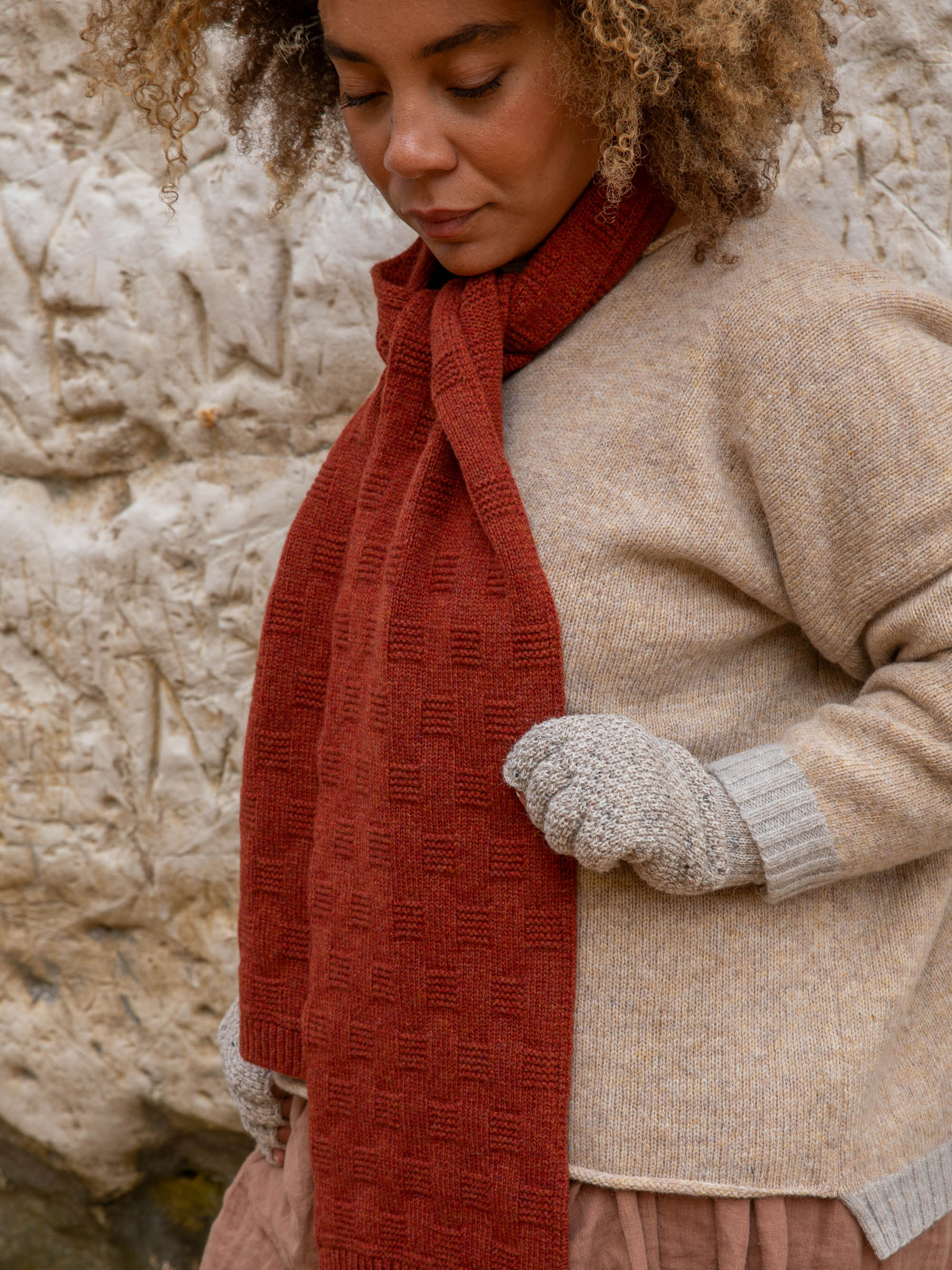 A rust-colored knitted scarf with a textured, grid-like pattern.
