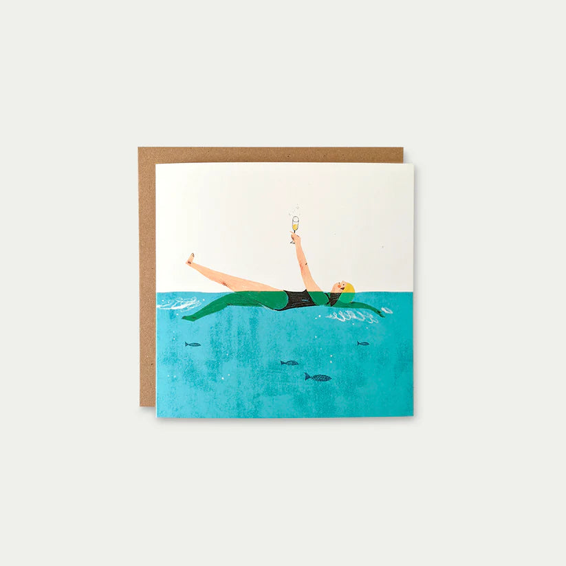 Greeting card illustration: Woman in a green swimsuit floats in turquoise water, holding a champagne glass aloft; small fish