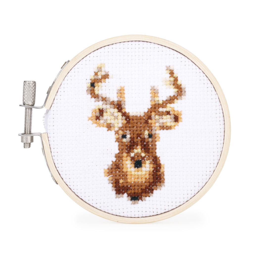 Cross-stitch embroidery of a deer head in brown and beige tones, displayed in a round wooden hoop.