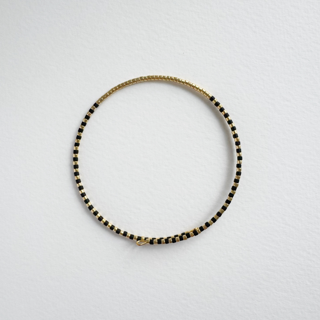 Black and gold beaded bracelet.  Circular design with small, square beads.  Simple clasp closure.