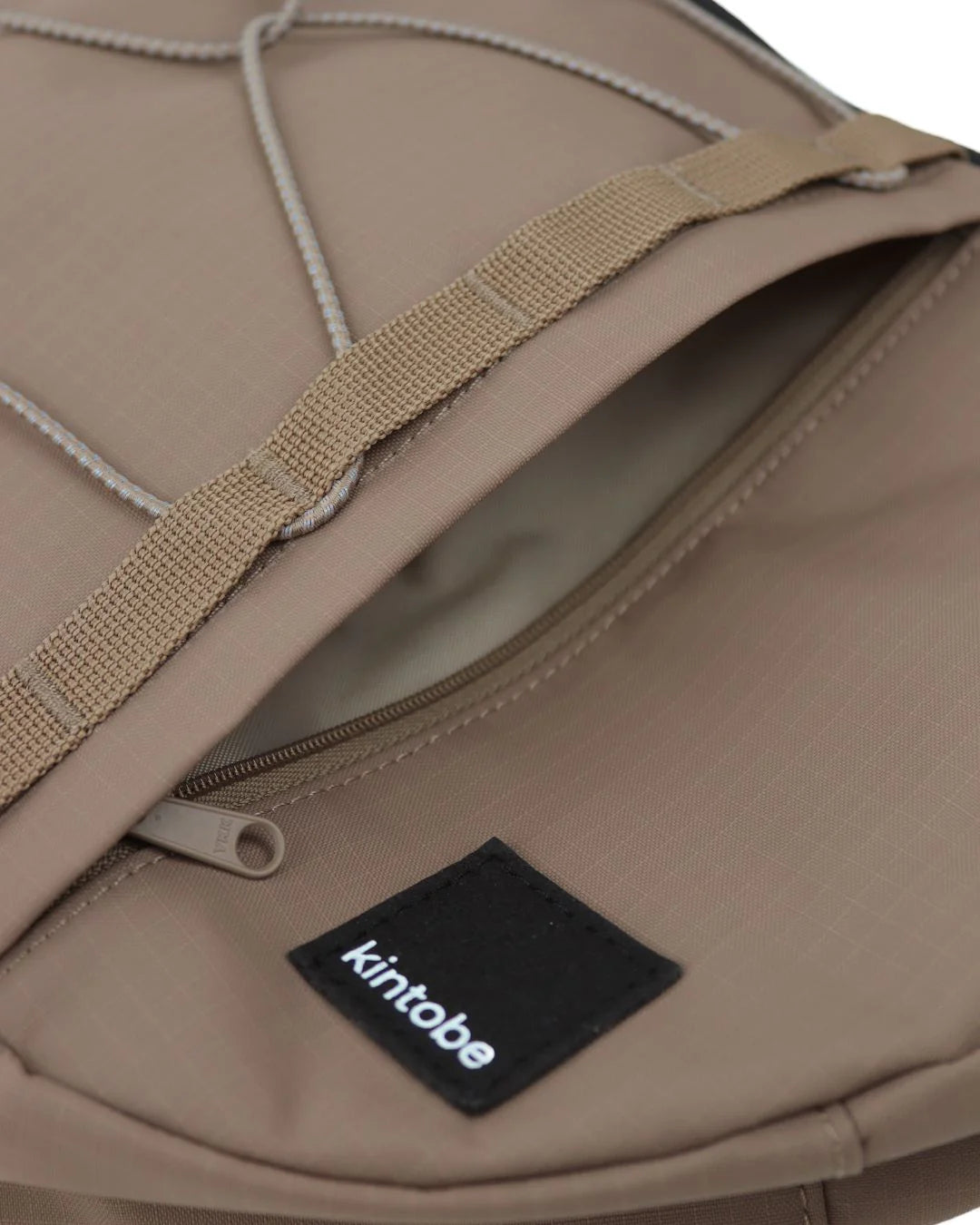Close-up of a taupe Kintobe bag's zippered pocket, showing beige straps and a black brand label.