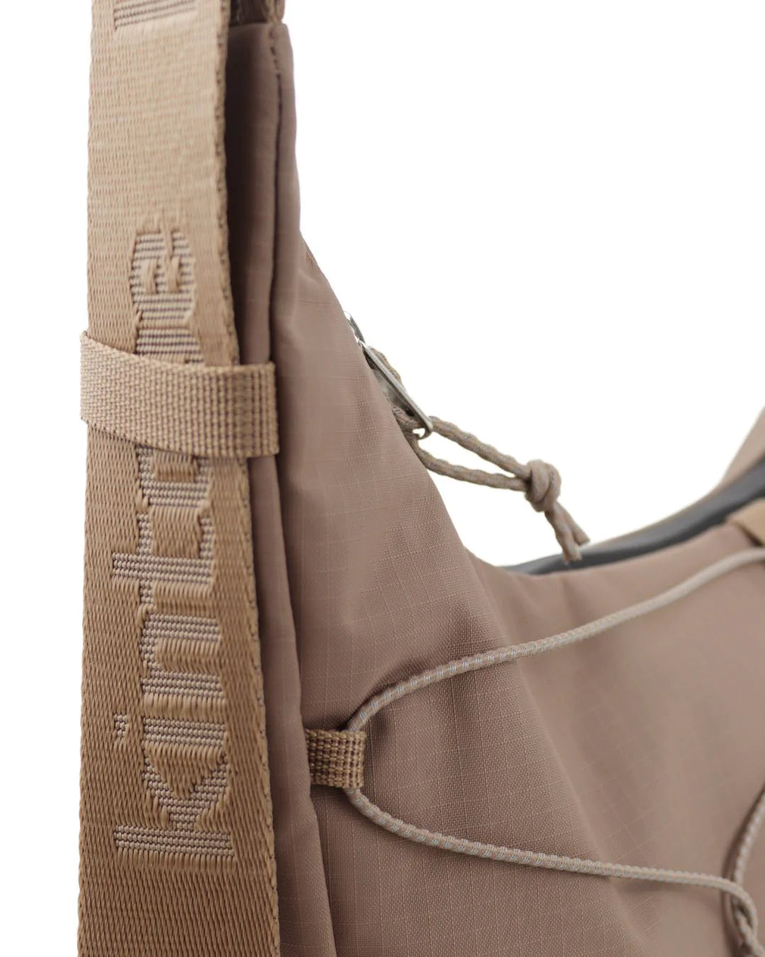 Tan crossbody bag with a textured fabric and adjustable shoulder strap featuring embossed branding.