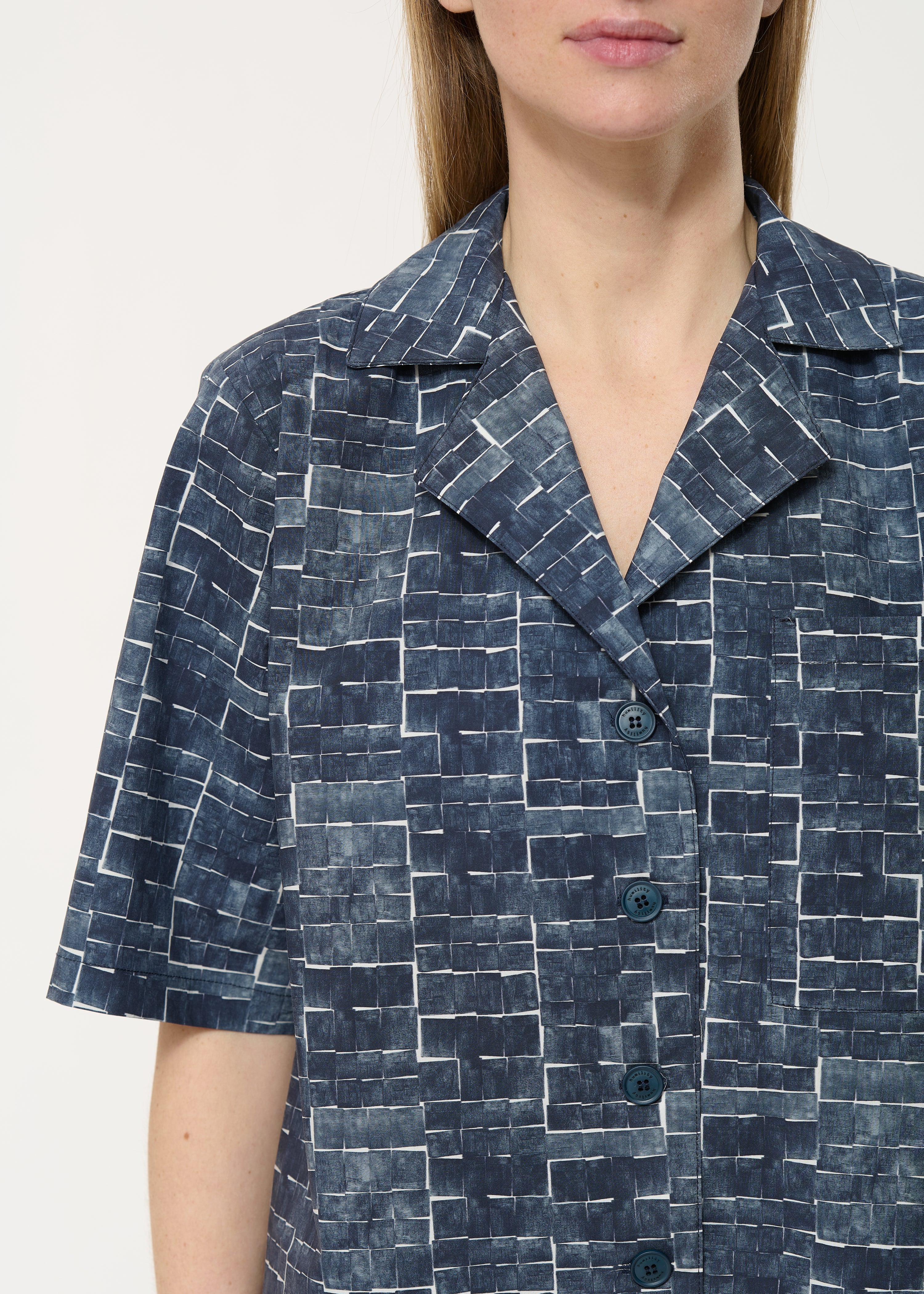 Close-up of a women's short-sleeved collared shirt featuring a dark blue and white abstract block print pattern.