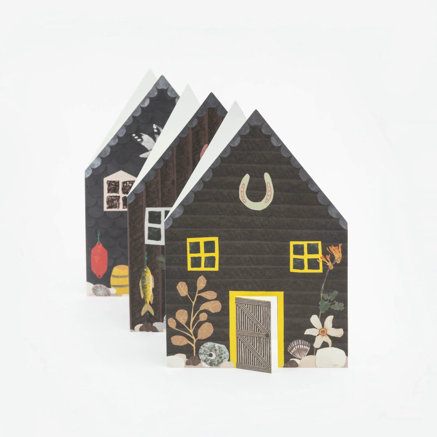 Three dark-grey paper houses with yellow accents, illustrated with nautical and floral details.
