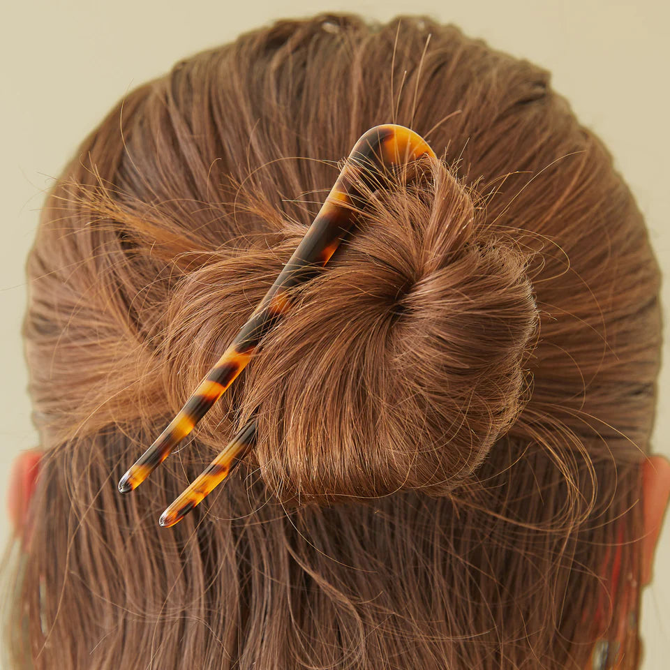 Close-up of a bun with a decorative hairpin against a neutral background