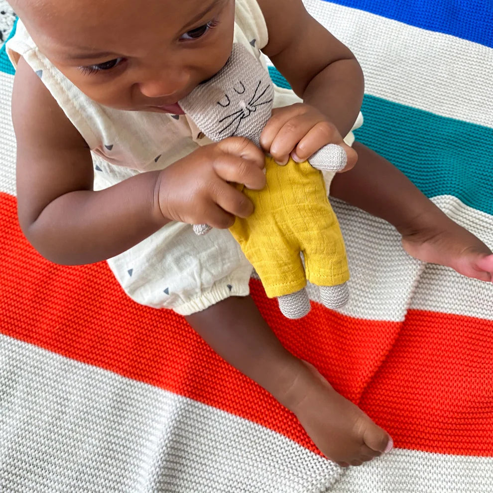 Baby holding a knitted cat toy wearing a yellow outfit.