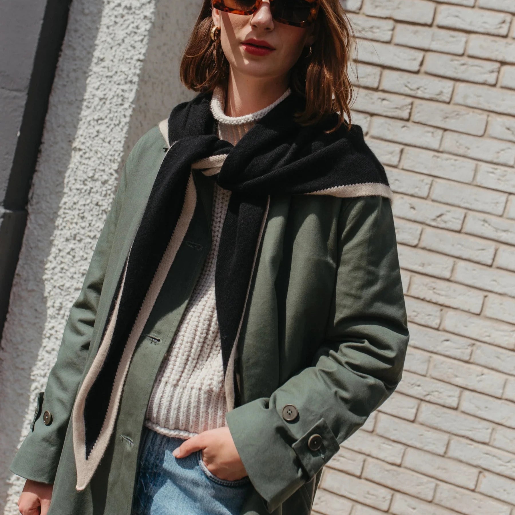 Olive green trench coat with a black and cream striped scarf draped around the neck.