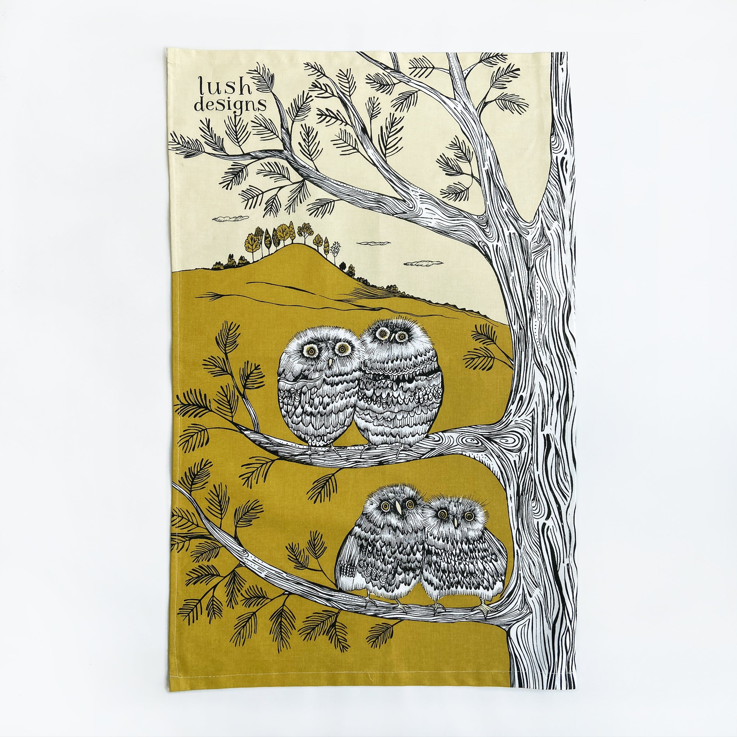 Lush Designs tea towel featuring a mustard yellow background, black line drawings of two pairs of owls perched on tree
