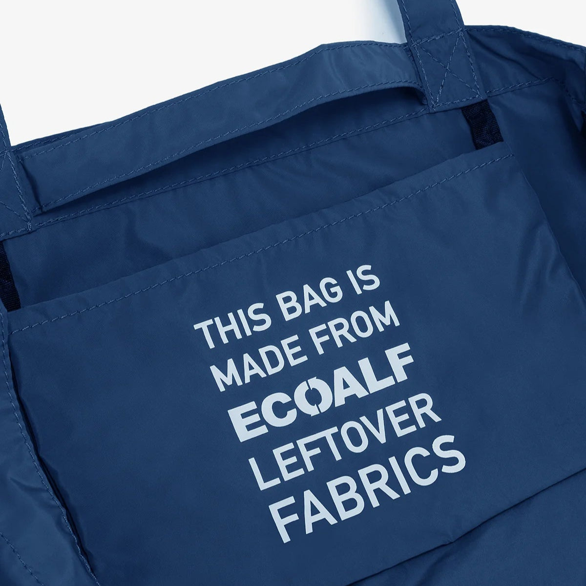 Dark blue tote bag with an exterior pocket displaying the text: "THIS BAG IS MADE FROM ECOALF LEFTOVER FABRICS".