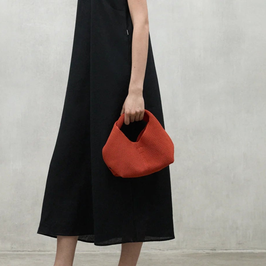 Small terracotta-colored woven handbag with a curved top and single top handle.