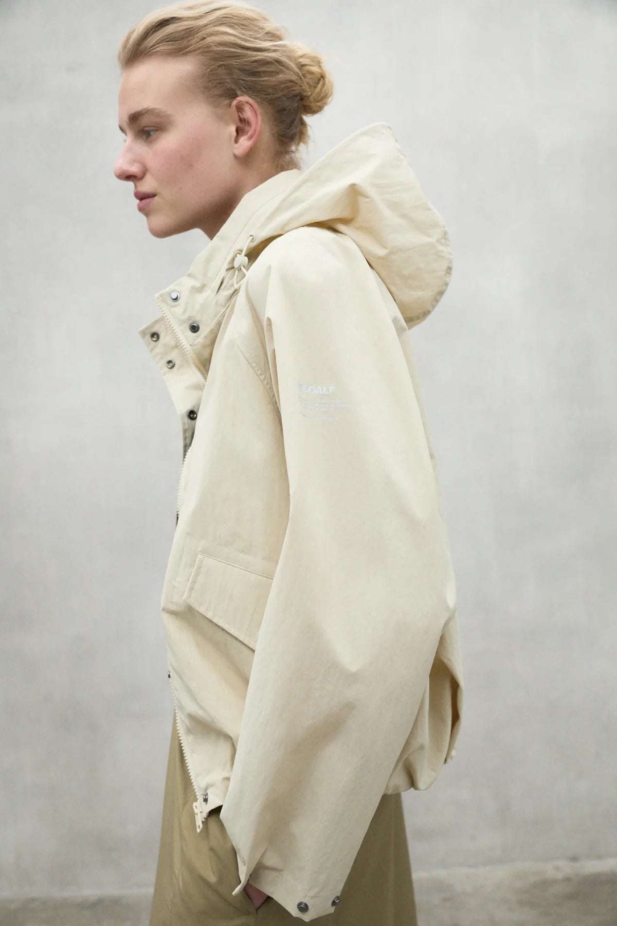 Cream-colored hooded jacket with snap closures and subtle branding on the sleeve.
