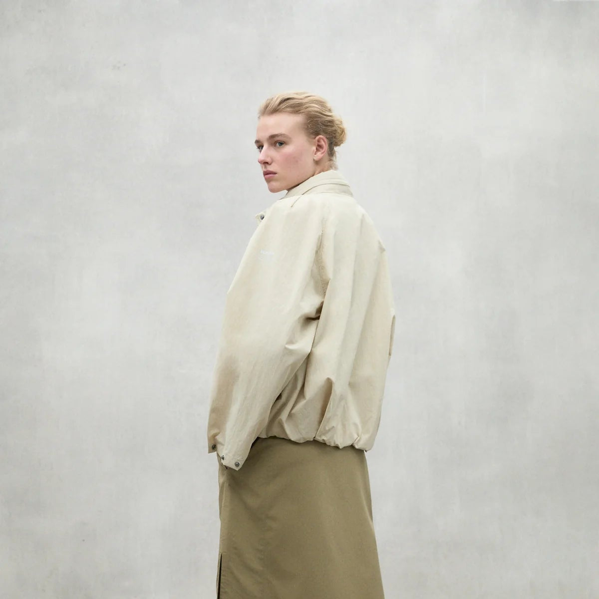 Beige oversized jacket with elastic waistband, shown from the back. The model is wearing a khaki skirt.
