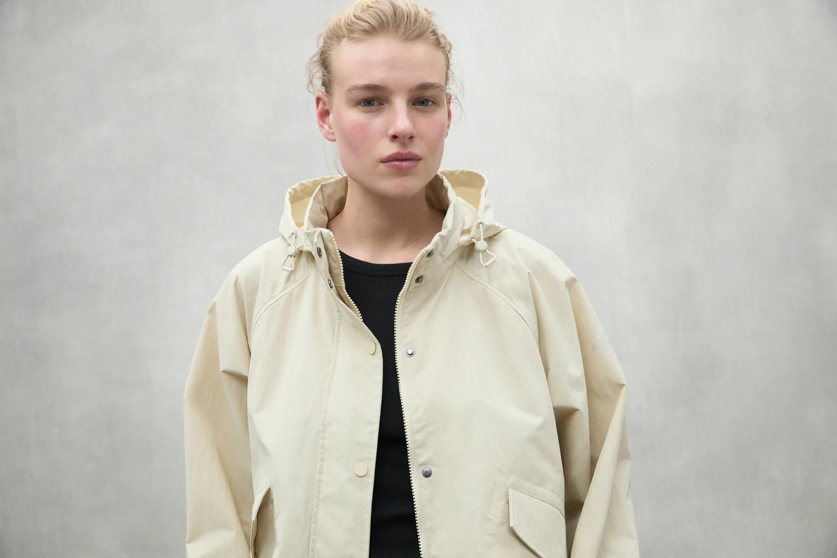 Cream-colored hooded jacket with button closure and patch pockets.