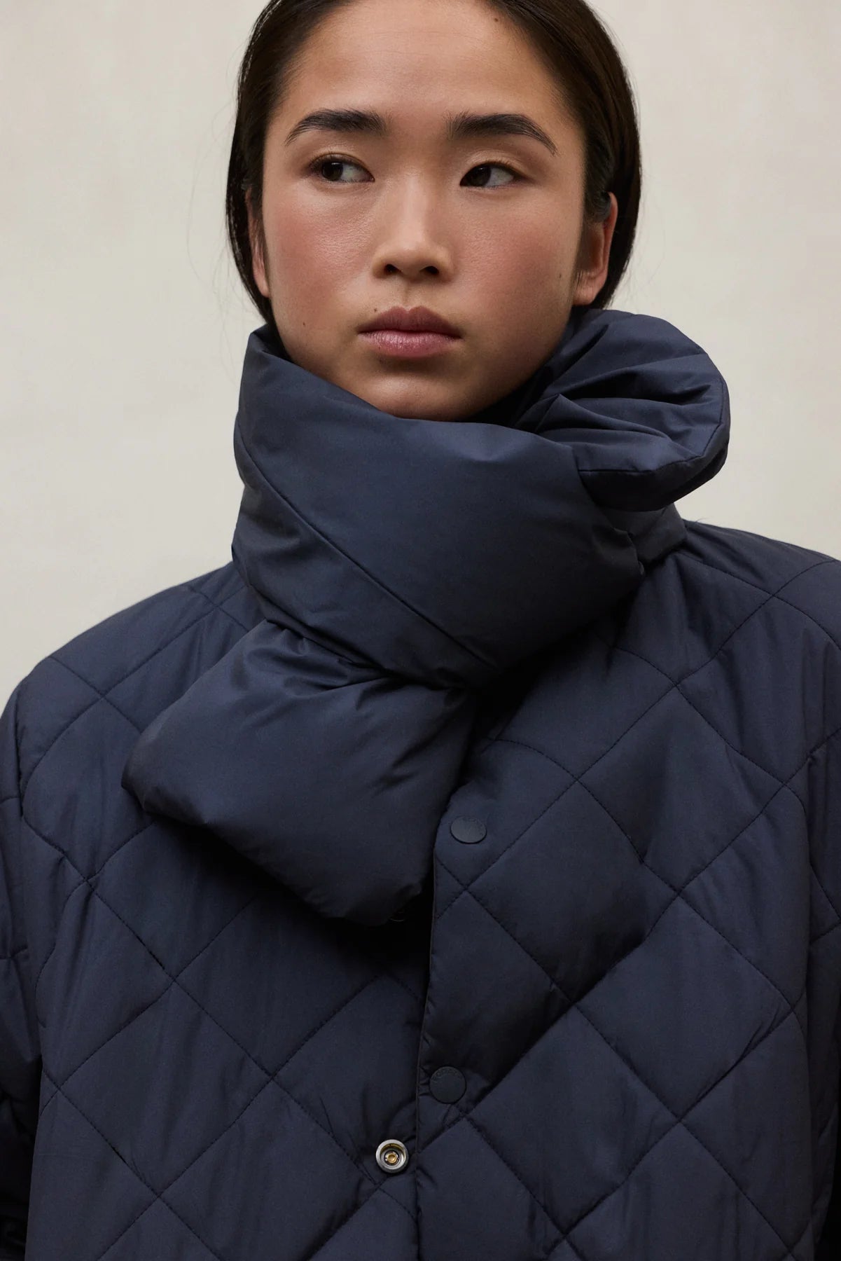 Person wearing a dark blue quilted jacket with a matching scarf against a neutral background