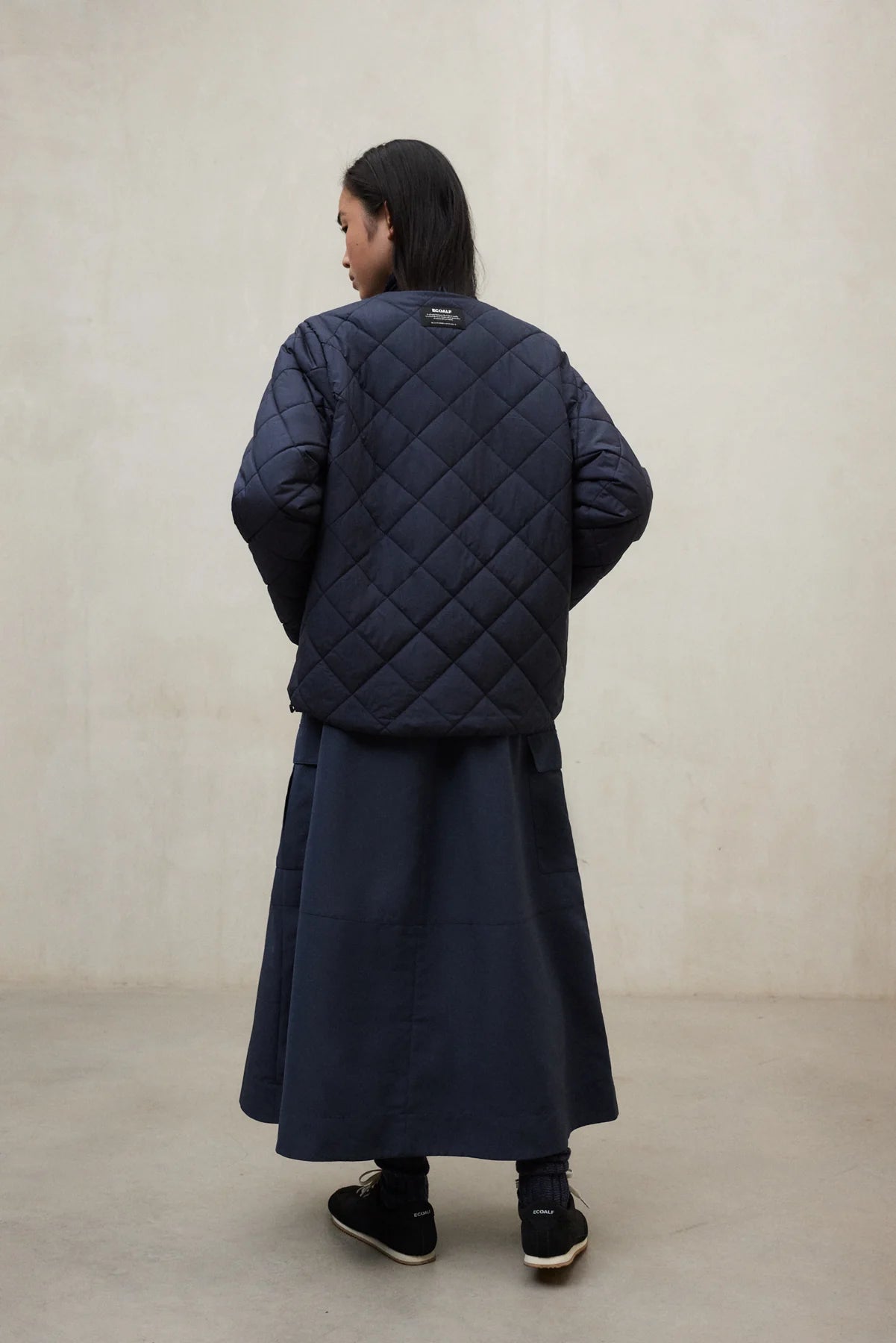 Person wearing a long navy quilted coat against a plain background