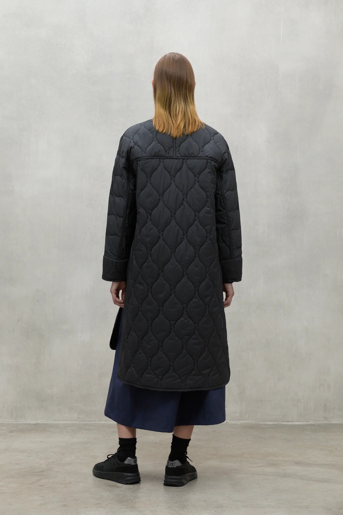 Black quilted longline coat with a diamond pattern. The coat has long sleeves and a relaxed fit.