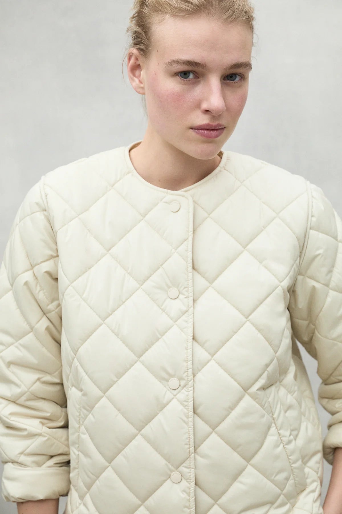 Cream-colored quilted jacket with a button front and diamond-shaped quilting pattern.