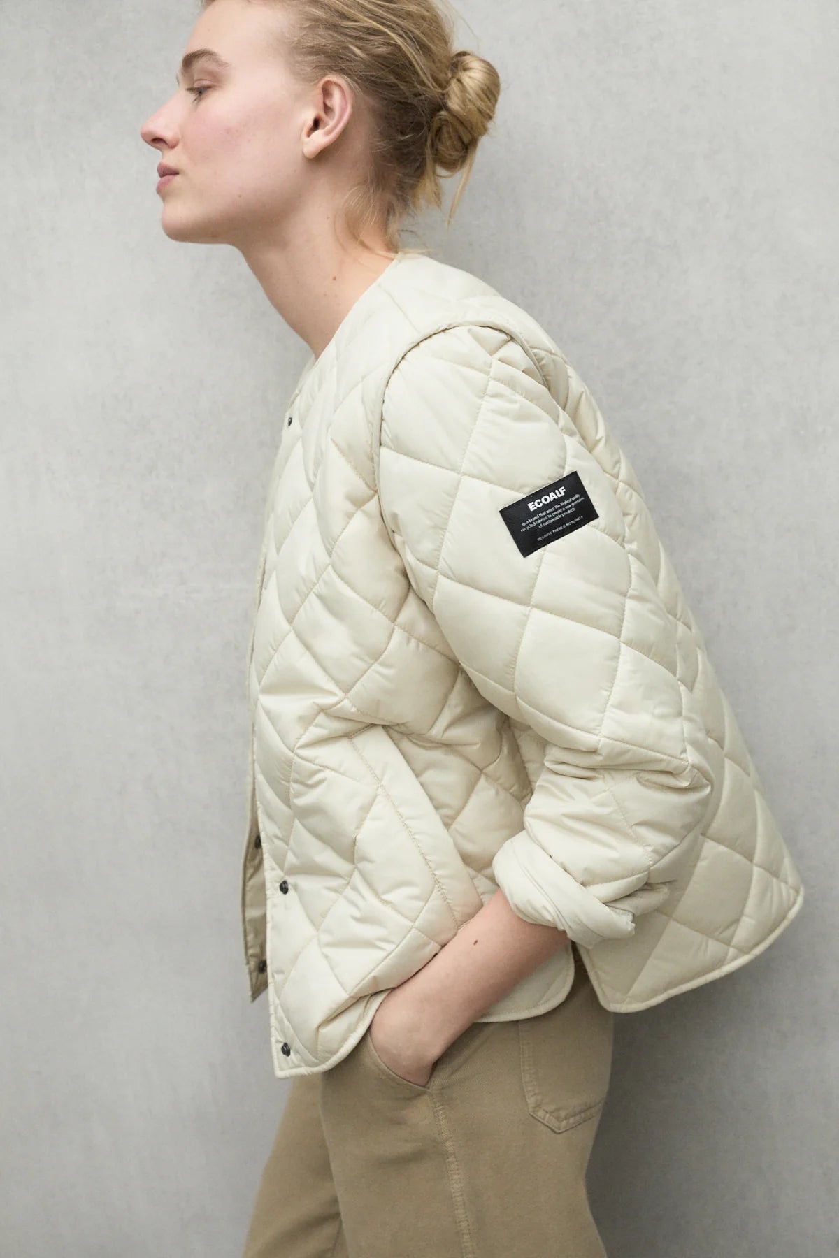 Cream-colored quilted jacket with a diamond pattern and a small black brand label on the sleeve.