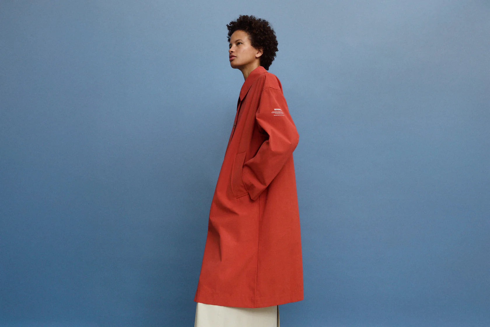 Long terracotta-colored raincoat with a collared neckline and pockets.