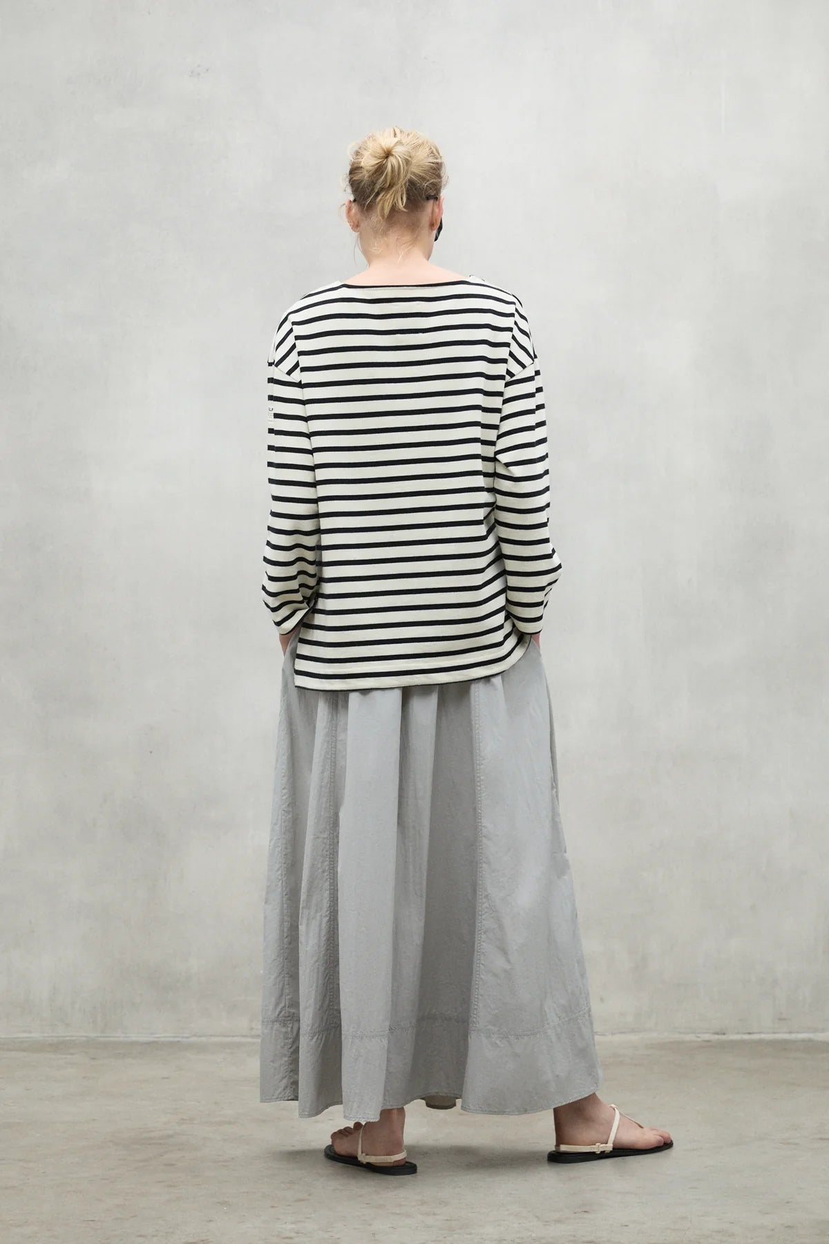 Woman's long gray skirt and black and white striped long-sleeved shirt viewed from behind.