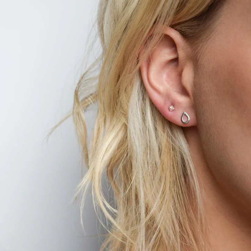 Pair of silver stud earrings; one is a small geometric shape, the other a teardrop.