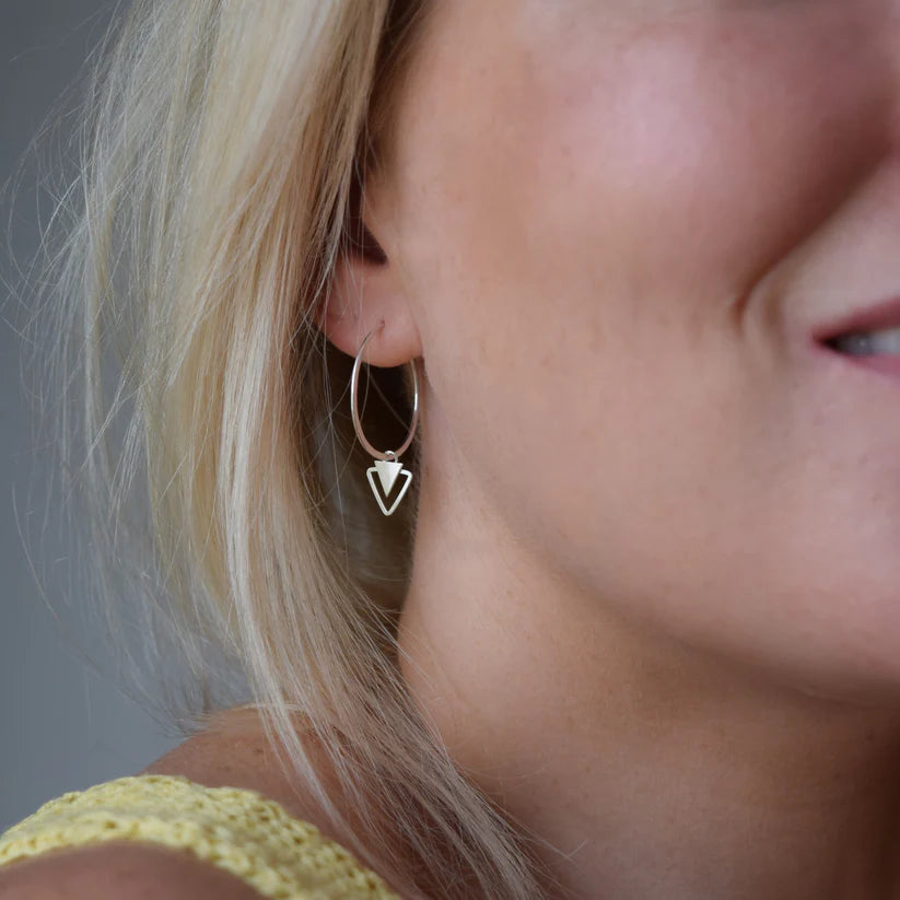 Silver hoop earrings with a small, double-triangle charm.