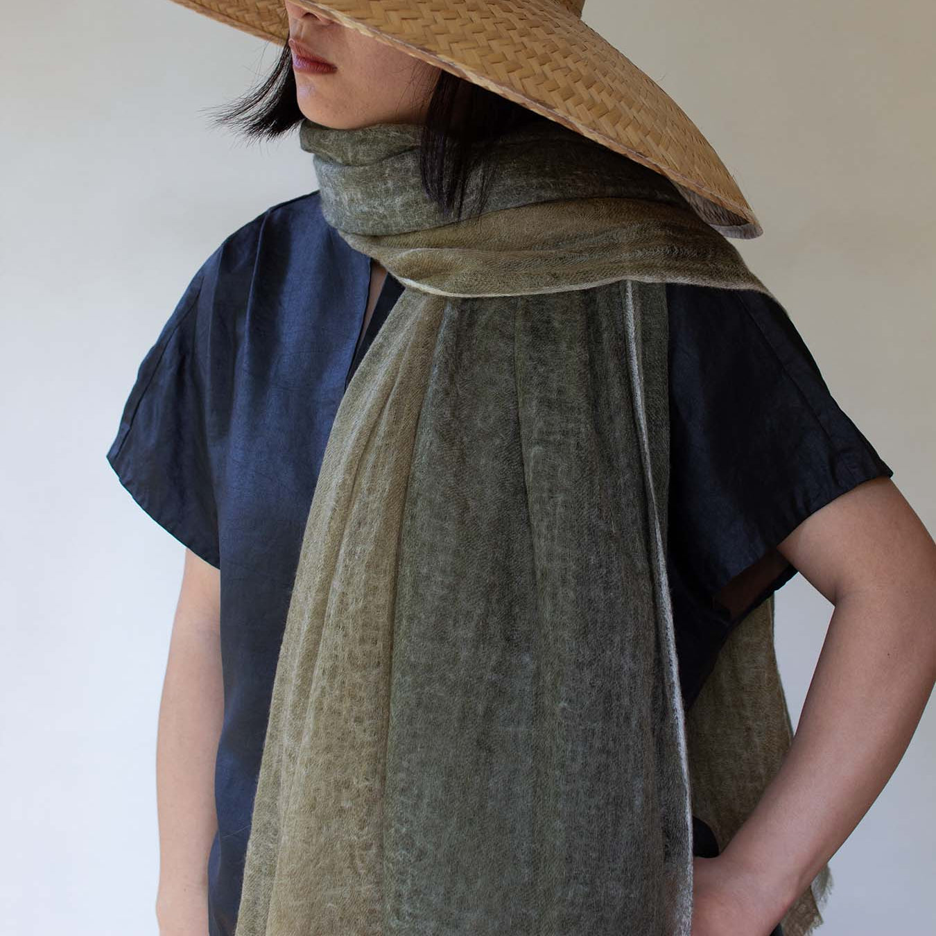 A person wearing a dip-dyed green cashmere scarf with a gradient of green and yellow tones, paired with a black top and a hat.