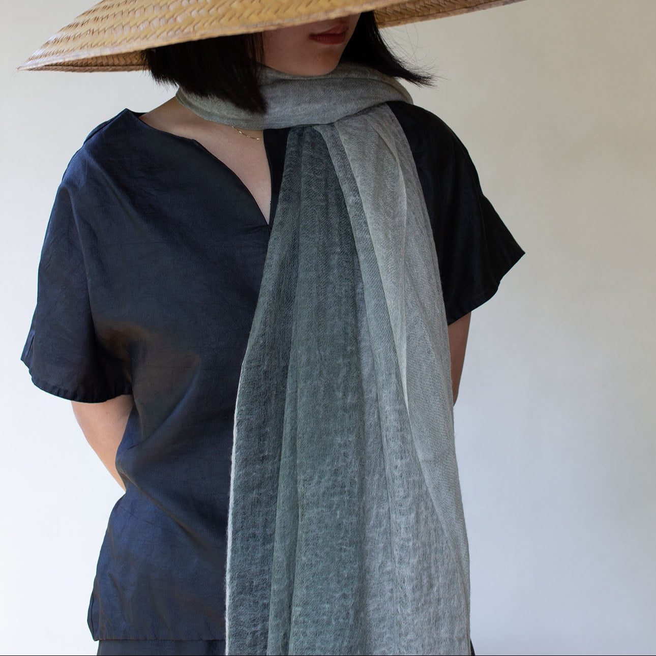 Person wearing a wide-brimmed straw hat and a light gray scarf against a plain background