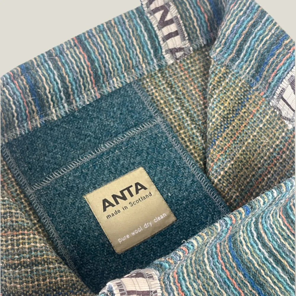 Close-up of an ANTA pure wool throw blanket, teal and multicolored, made in Scotland; label visible.